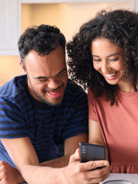 Disabled man with down syndrome laughing with support worker at something on phone