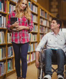 Disabled man in wheelchair with carer in library
