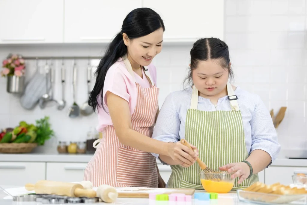 Support worker with disabled girl in kitchen teaching her how to cook